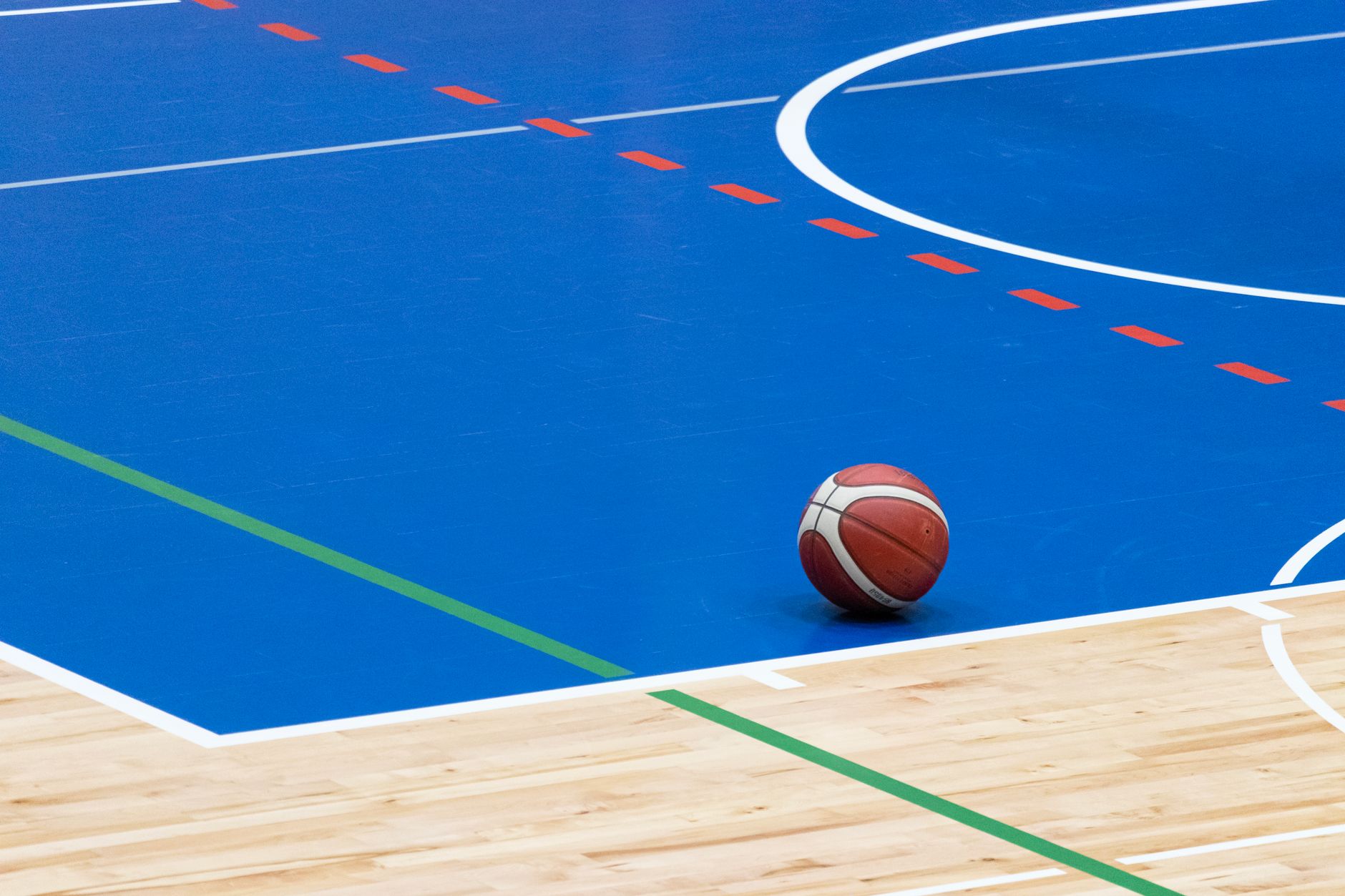 A basketball rests on a vibrant blue indoor court with wood flooring and colorful lines in Allen, TX
