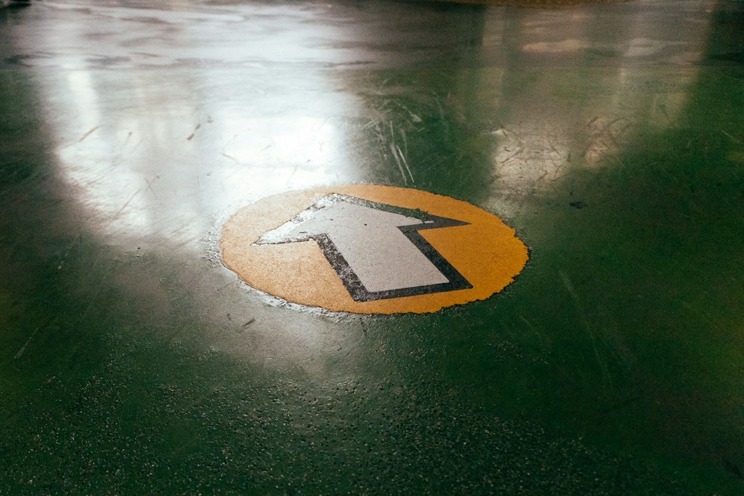 A yellow and black arrow sign sitting on top of a green floor in Allen, TX